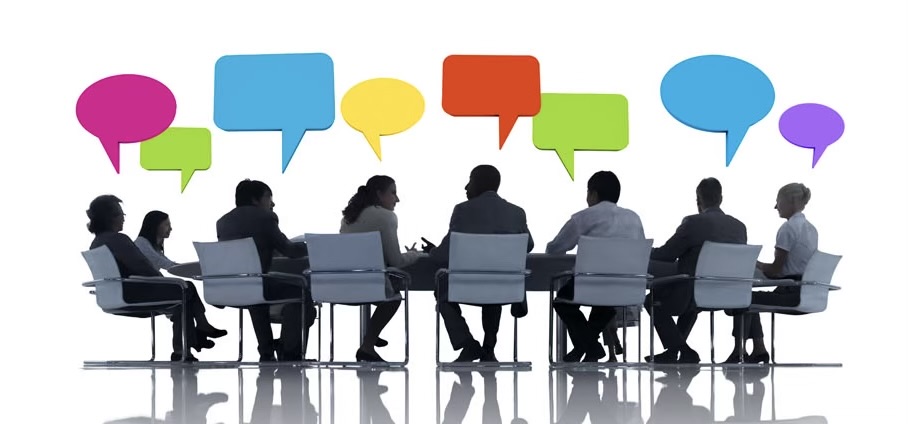 a black and white drawing of seven professionals sitting around a conference table. Above their heads are empty colored comment boxes.