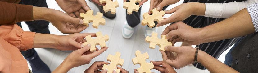 A photo of people in a circle with only thier hands showing.  There is a puzzle piece in each hand.